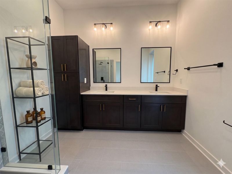This modern bathroom features dark wood cabinetry, dual sinks with sleek black fixtures, and ample counter space. It includes a glass-enclosed shower and open shelving for storage, enhanced by stylish lighting and neutral tile flooring.