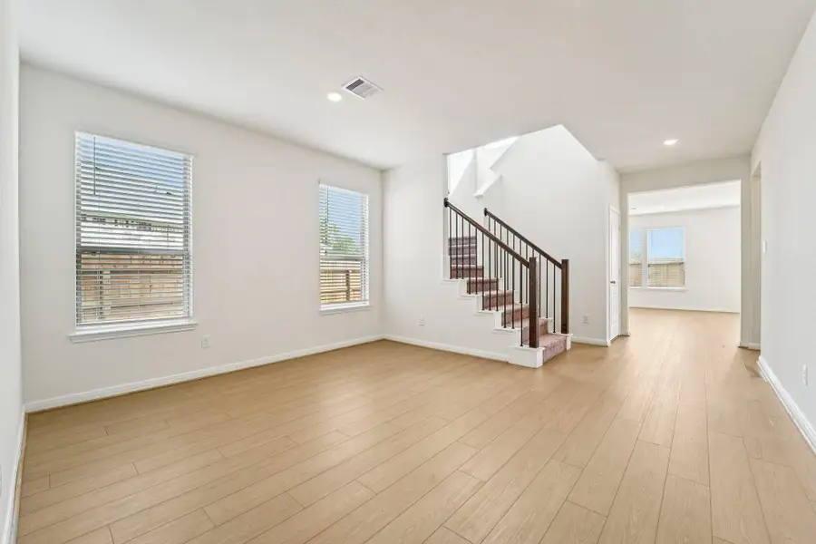 Just beyond the generous entryway, this Flex room awaits. It is highlighted by Bandera vinyl plank flooring in Toasted Sienna, large windows with privacy blinds, custom neutral paint, and recessed lighting.