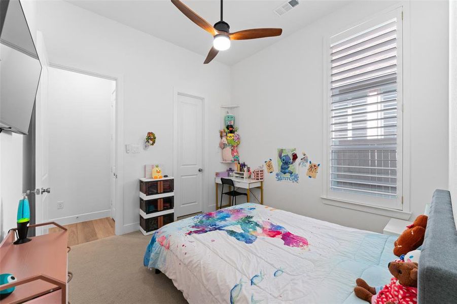 The room features a ceiling fan with light, a window with horizontal blinds, and light-colored carpeting