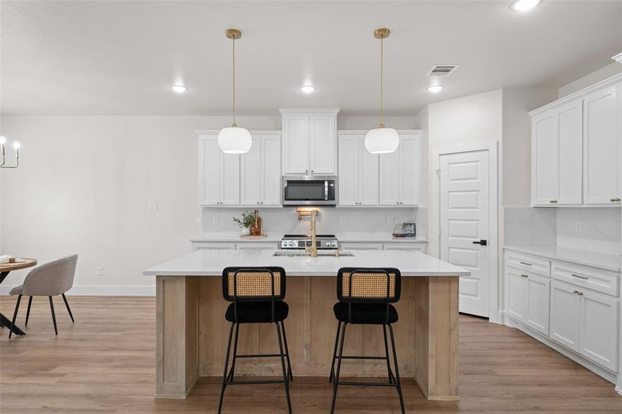 Kitchen featuring appliances with stainless steel finishes, light wood-type flooring, a center island with sink, a kitchen bar, and light countertops Kitchen featuring appliances with stainless steel finishes, light wood-type flooring, a center island with sink, a kitchen bar, and light countertops