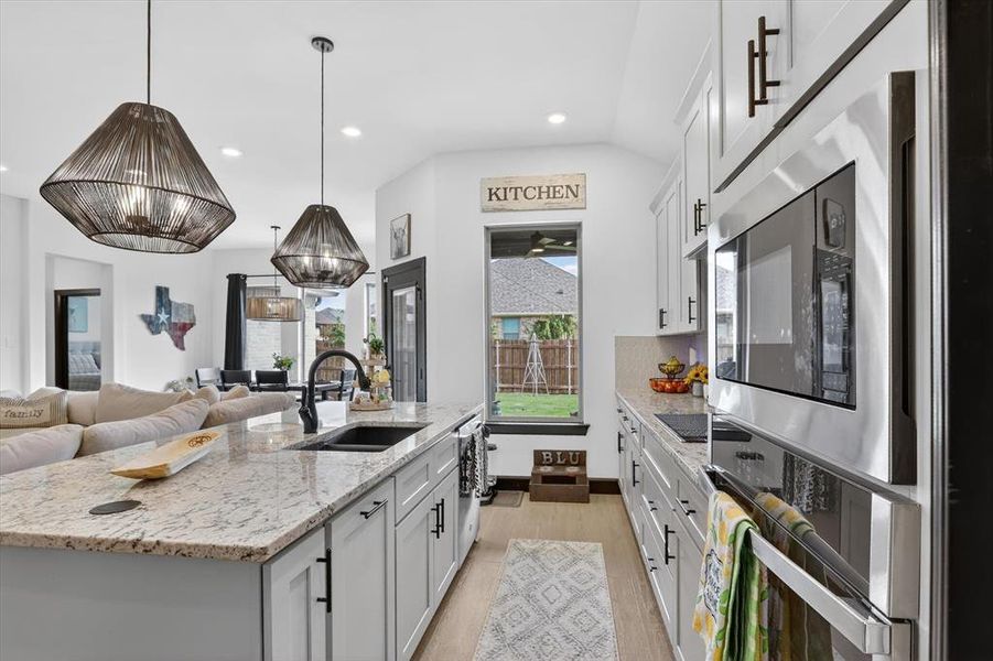 Open-concept kitchen featuring light-toned cabinetry, a spacious island with a granite countertop, and modern pendant lighting