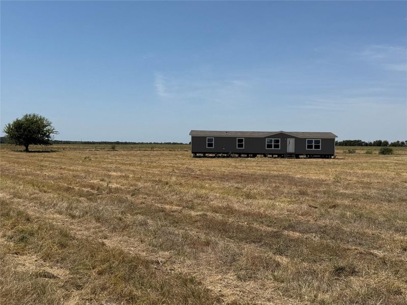 An expansive open pasture surrounds this classic manufactured home set against a clear blue sky.