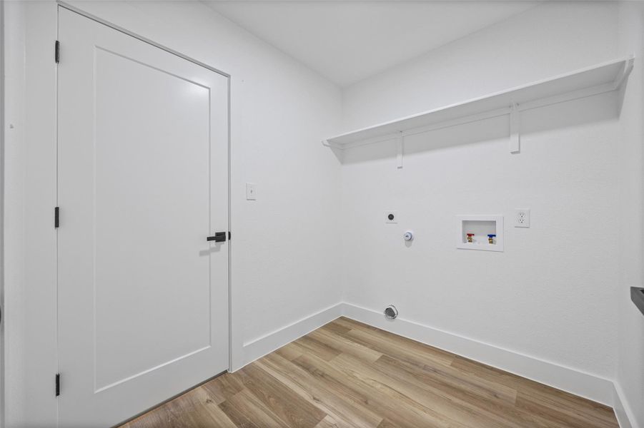 Dedicated utility space located upstairs featuring wood-finish flooring, crisp white walls, and a convenient wall-mounted shelf Dedicated utility space located upstairs featuring wood-finish flooring, crisp white walls, and a convenient wall-mounted shelf