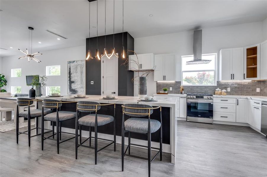 Kitchen featuring appliances with stainless steel finishes, a center island, wall chimney exhaust hood, and light hardwood / wood-style flooring