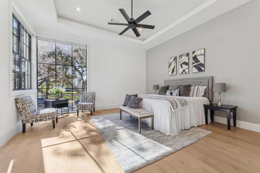 This first-floor secondary bedroom features large windows allowing abundant natural light, high ceilings with recessed lighting, and light wood flooring. The neutral color palette enhances its airy and inviting atmosphere.