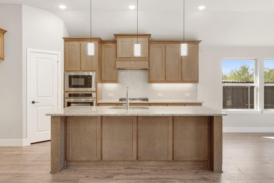 Kitchen with large island, granite countertops, light wood cabinets, pendant lights, and stainless steel appliances
