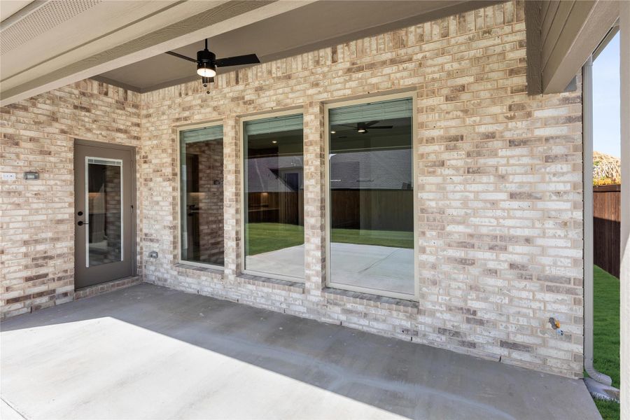 Covered back patio with ceiling fan, concrete floor, and large windows on brick exterior wall