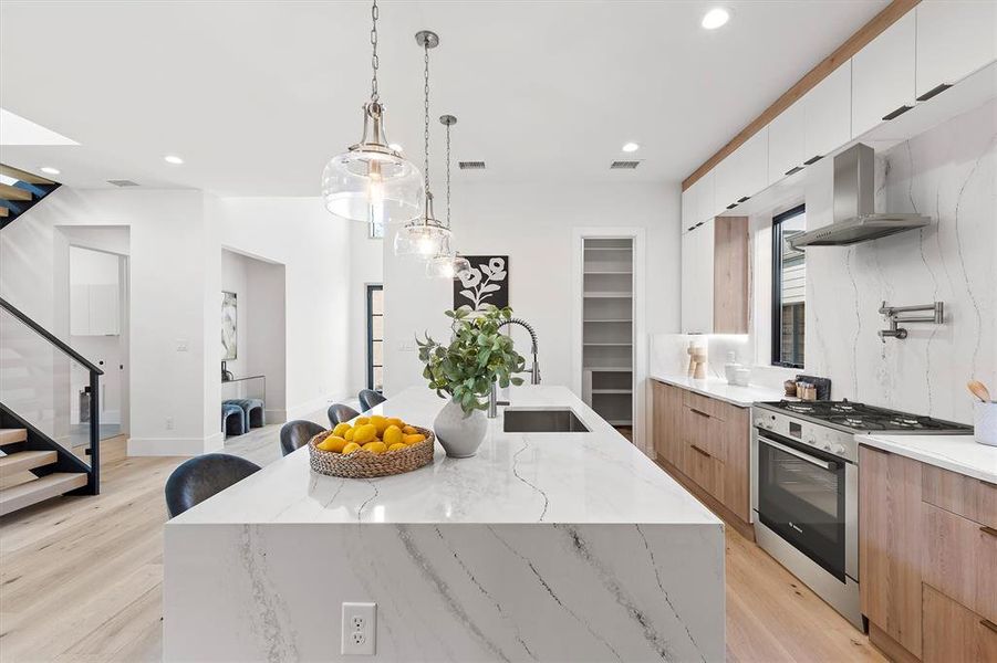 Kitchen with pendant lighting, a large island with sink, white cabinetry, light hardwood / wood-style flooring, and high end range