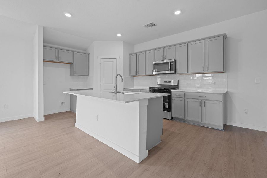 Kitchen with gray cabinets, appliances with stainless steel finishes, tasteful backsplash, an island with sink, and light wood-style floors Kitchen with gray cabinets, appliances with stainless steel finishes, tasteful backsplash, an island with sink, and light wood-style floors