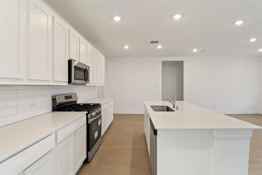 Kitchen with stainless steel appliances, white cabinetry, light wood-style floors, a center island with sink, and recessed lighting