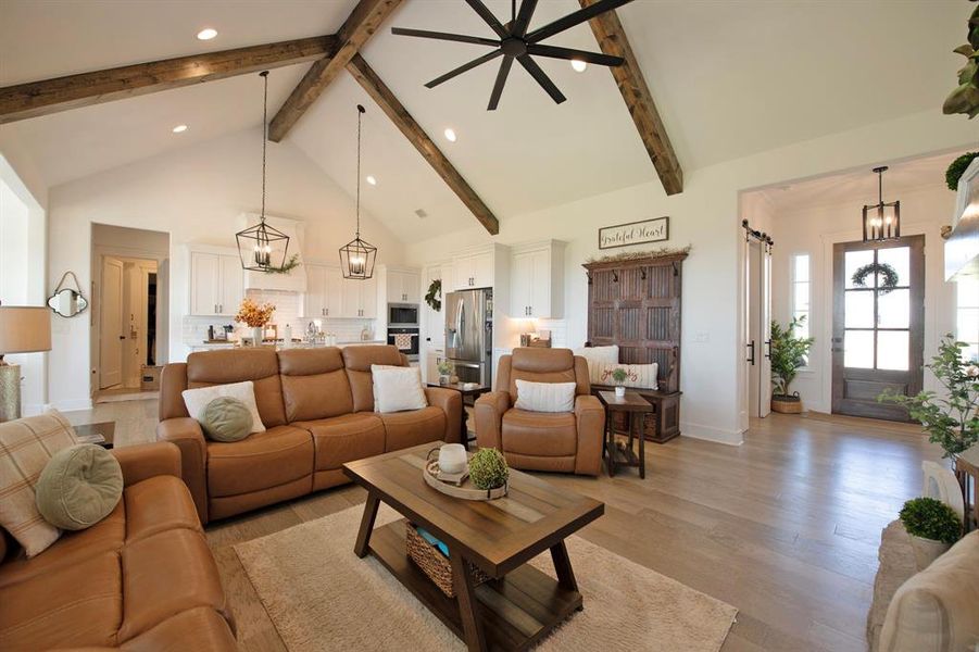 Living room with a chandelier, high vaulted ceiling, light wood-style flooring, beamed ceiling, and recessed lighting