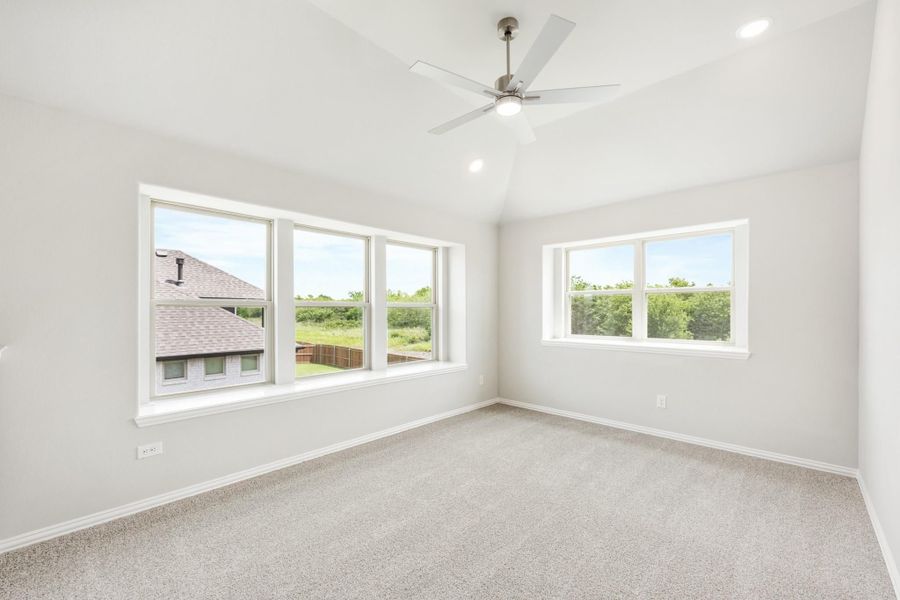 Empty bedroom with carpet flooring, ceiling fan, vaulted ceiling, and large windows with backyard views Empty bedroom with carpet flooring, ceiling fan, vaulted ceiling, and large windows with backyard views