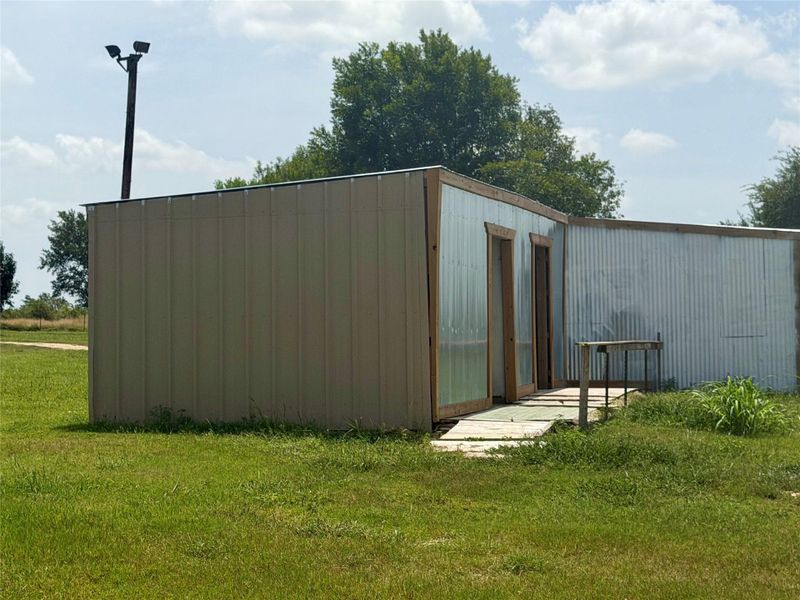 A utilitarian outbuilding, featuring a simple metal construction, sits amidst a verdant landscape.