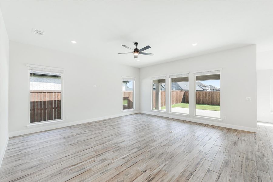 Empty living room with wood-look tile floors, ceiling fan, and large windows overlooking backyard