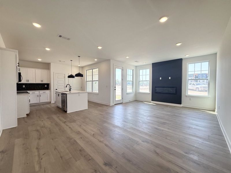 Kitchen with white cabinets, open floor plan, a center island with sink, hanging light fixtures, and light wood-style floors