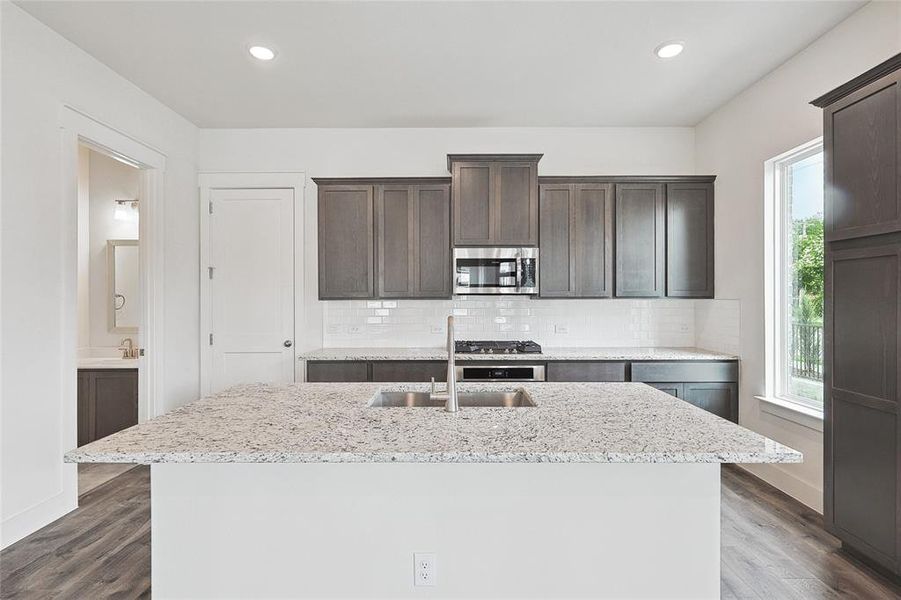 Kitchen featuring decorative backsplash, dark brown cabinetry, sink, and a center island with sink