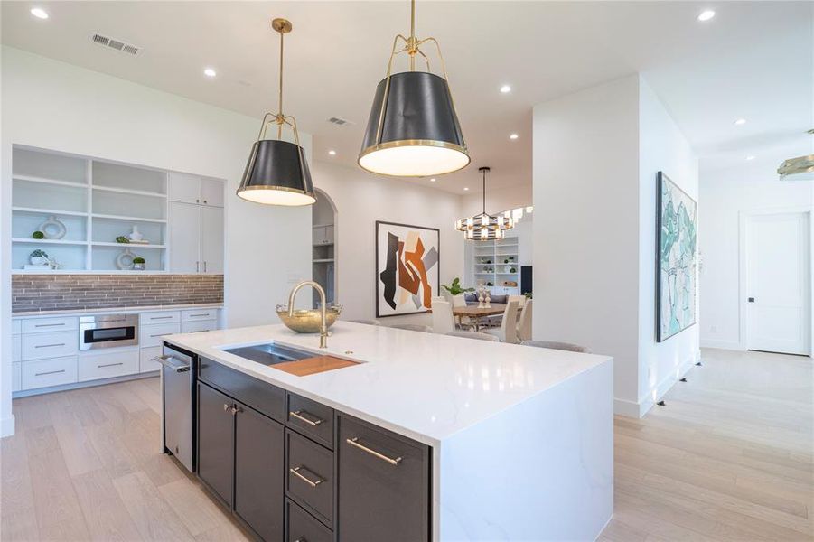 Kitchen with sink, an island with sink, light hardwood / wood-style floors, decorative light fixtures, and white cabinets