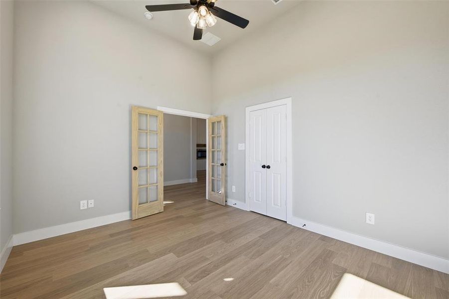 Unfurnished bedroom featuring french doors, wood finished floors, a ceiling fan, a towering ceiling, and a closet