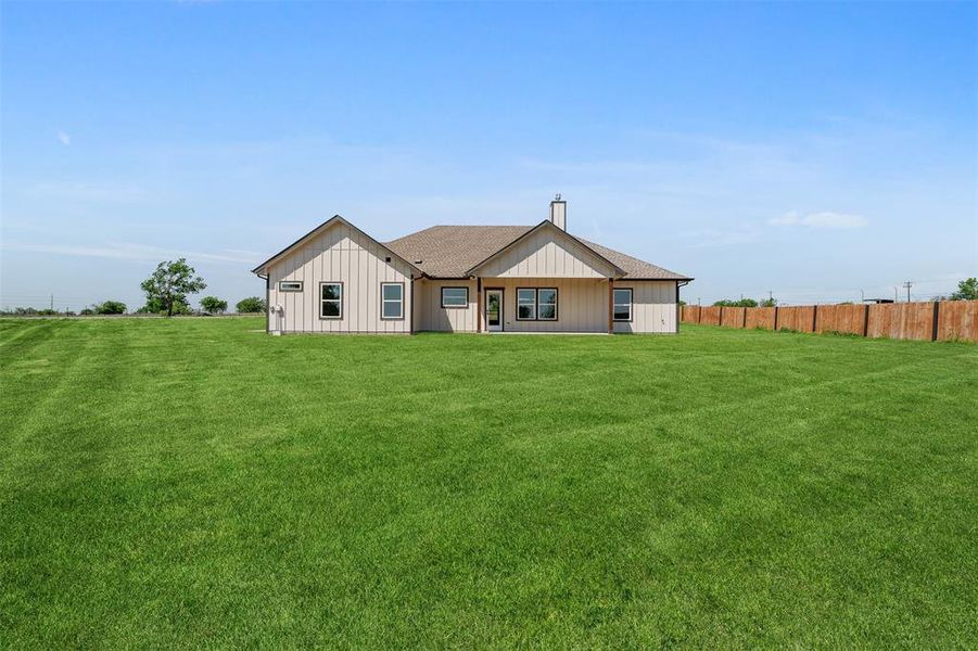 Rear view of property featuring a yard, roof with shingles, a chimney, and fence