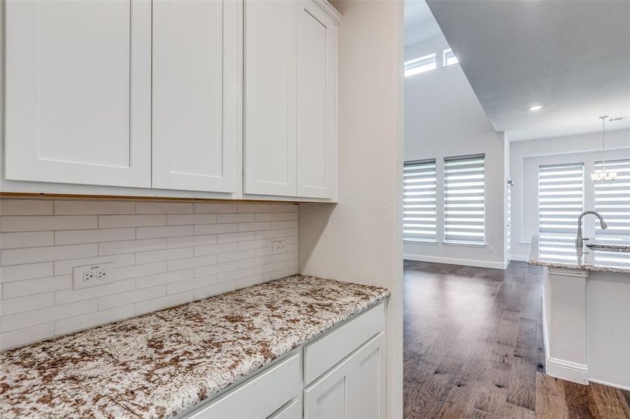 Kitchen with decorative backsplash, wood finished floors, white cabinets, baseboards, and light stone counters