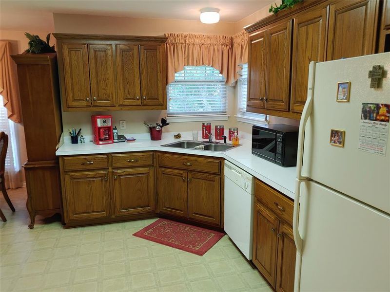 L-shaped kitchen featuring wood-finish cabinetry, white countertops, a double basin stainless steel sink, and light-toned flooring