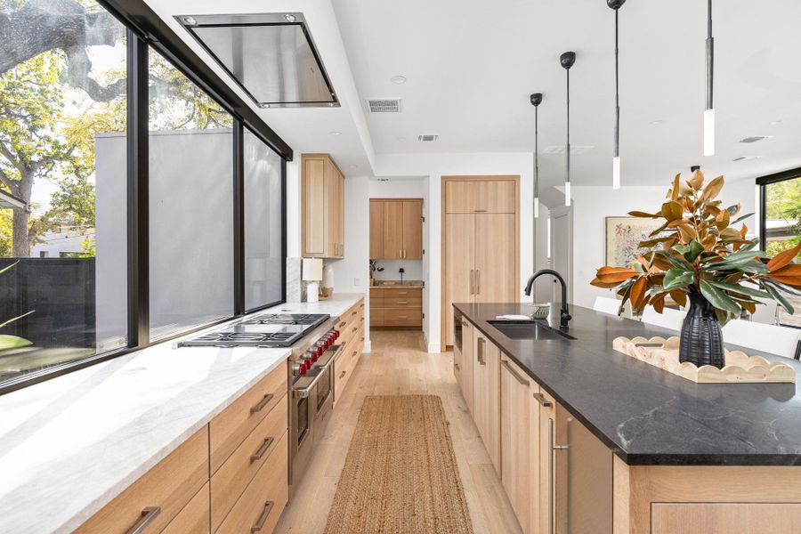 Kitchen with dark stone countertops, light wood finished floors, range with two ovens, decorative light fixtures, and recessed lighting Kitchen with dark stone countertops, light wood finished floors, range with two ovens, decorative light fixtures, and recessed lighting