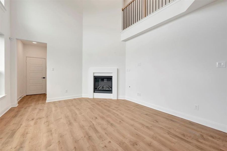 Unfurnished living room featuring a high ceiling, a glass covered fireplace, and light wood finished floors