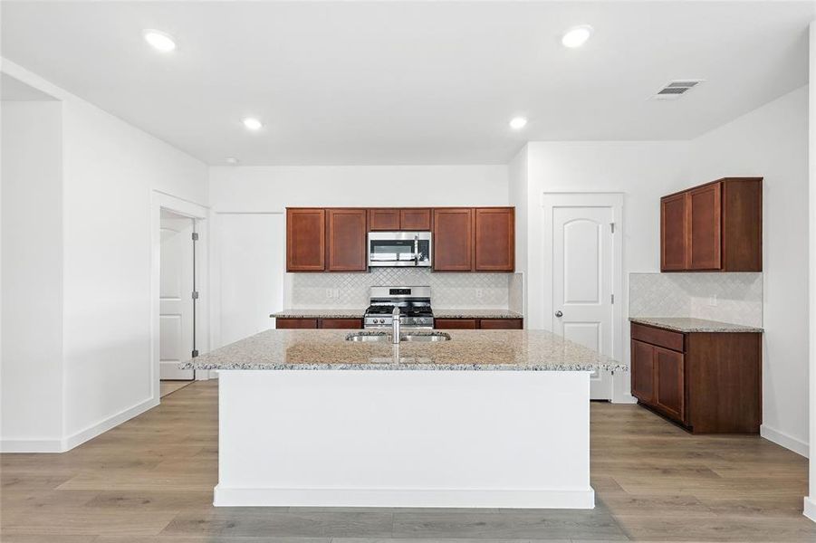 Kitchen with light stone countertops, tasteful backsplash, appliances with stainless steel finishes, recessed lighting, and an island with sink Kitchen with light stone countertops, tasteful backsplash, appliances with stainless steel finishes, recessed lighting, and an island with sink