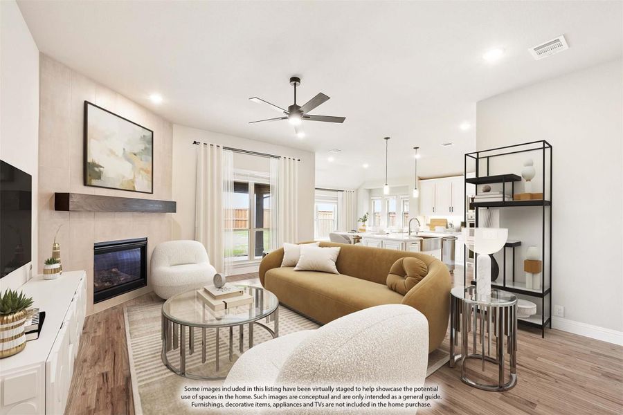 Open living room with tile fireplace, ceiling fan, hardwood floors, and open kitchen in background Open living room with tile fireplace, ceiling fan, hardwood floors, and open kitchen in background