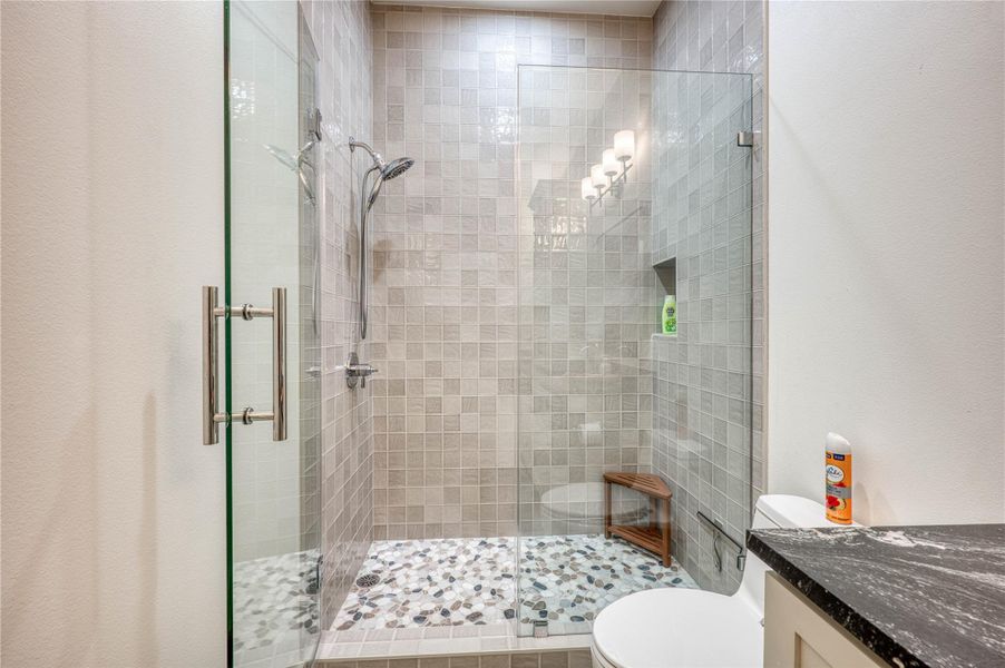 Glass-enclosed shower with mosaic wall tiling and pebble flooring