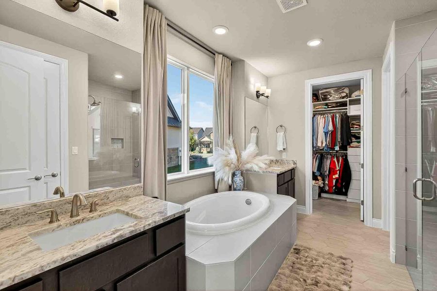 Bathroom featuring two vanities, a garden tub, a shower stall, a walk in closet, and recessed lighting