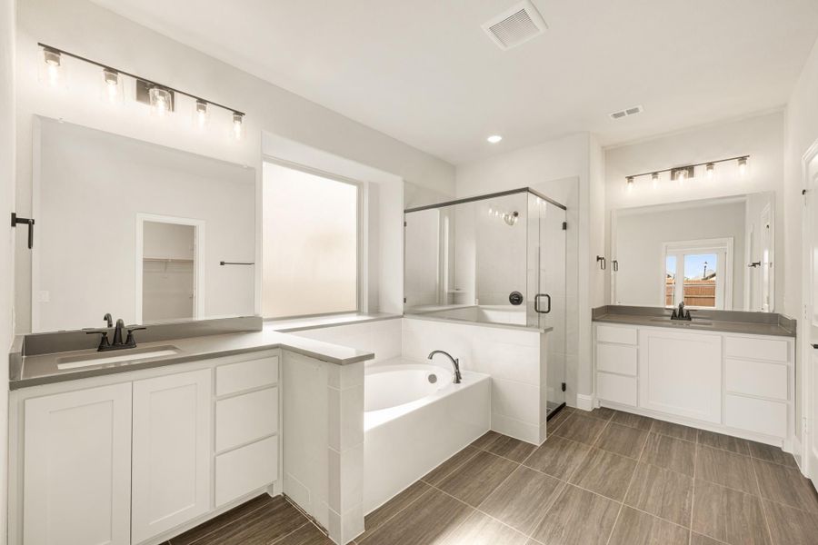 Master bathroom with dual vanities, soaking tub, glass shower, and wood-look tile floors
