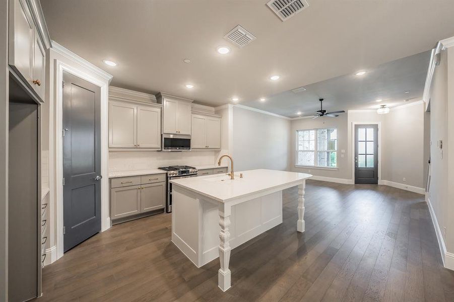 Kitchen featuring a large central island with turned legs, white countertops, and a gold-finish faucet