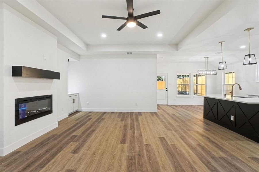 Unfurnished living room featuring a glass covered fireplace, a raised ceiling, light wood-style floors, and recessed lighting Unfurnished living room featuring a glass covered fireplace, a raised ceiling, light wood-style floors, and recessed lighting
