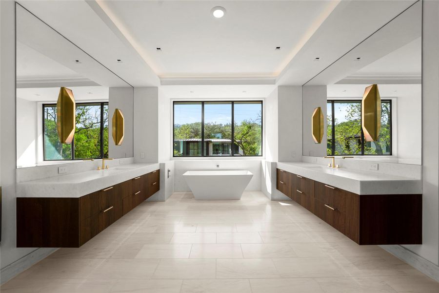 Primary bathroom featuring two vanities, a tray ceiling, a freestanding tub, and plenty of natural light