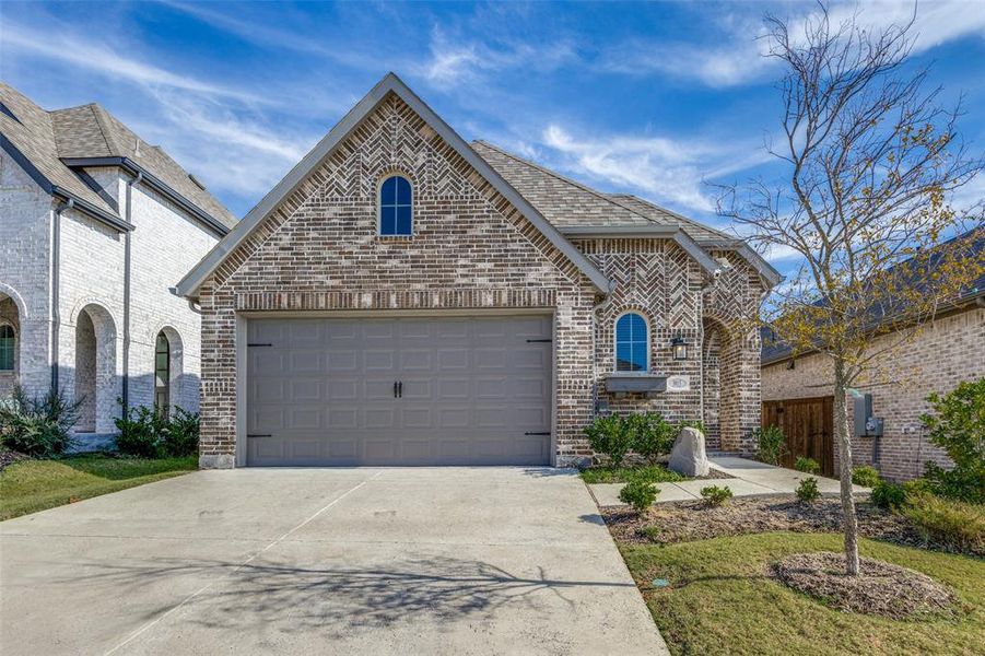 French country home with driveway, brick siding, and a garage
