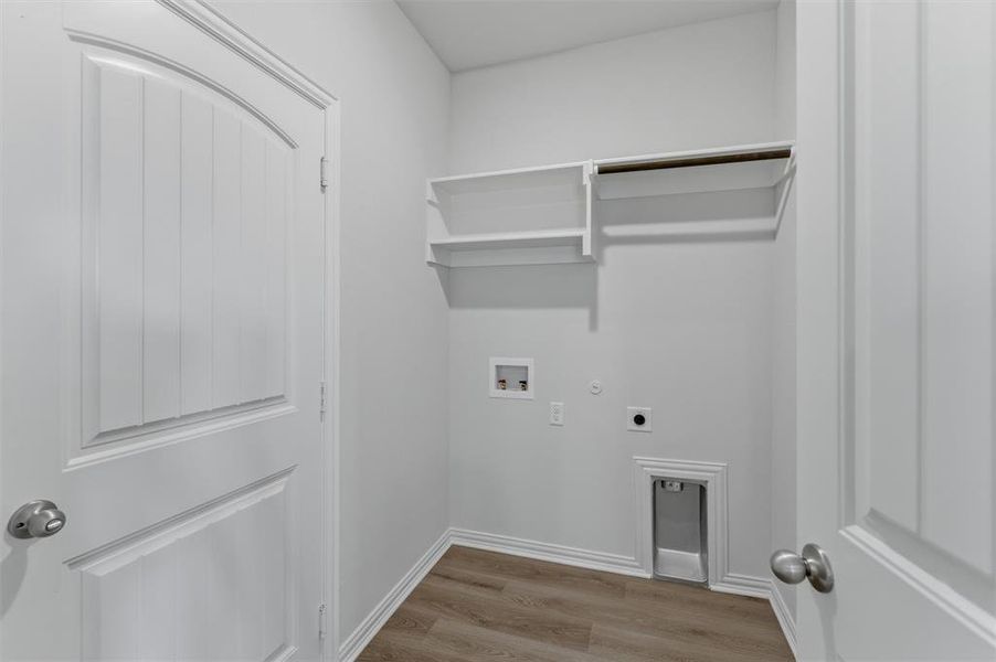 Dedicated utility room featuring wood-finish flooring, white walls, built-in shelving, a clothes hanging rod, and a laundry hookup