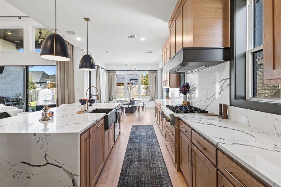 Kitchen with light stone counters, light wood finished floors, brown cabinets, a chandelier, and recessed lighting Kitchen with light stone counters, light wood finished floors, brown cabinets, a chandelier, and recessed lighting