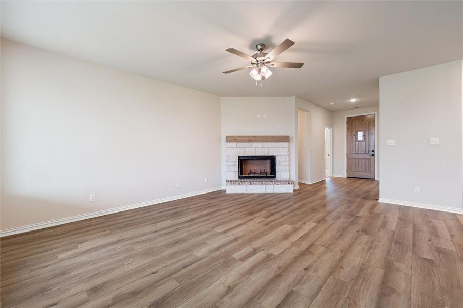 Unfurnished living room with light wood-style floors, a stone fireplace, and ceiling fan
