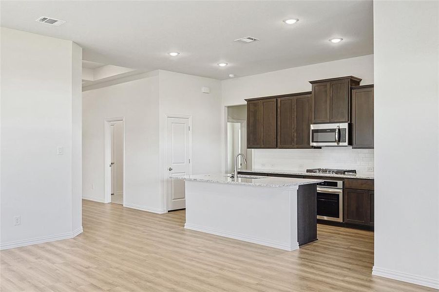 Kitchen featuring sink, stainless steel appliances, light hardwood / wood-style floors, a center island with sink, and dark brown cabinets