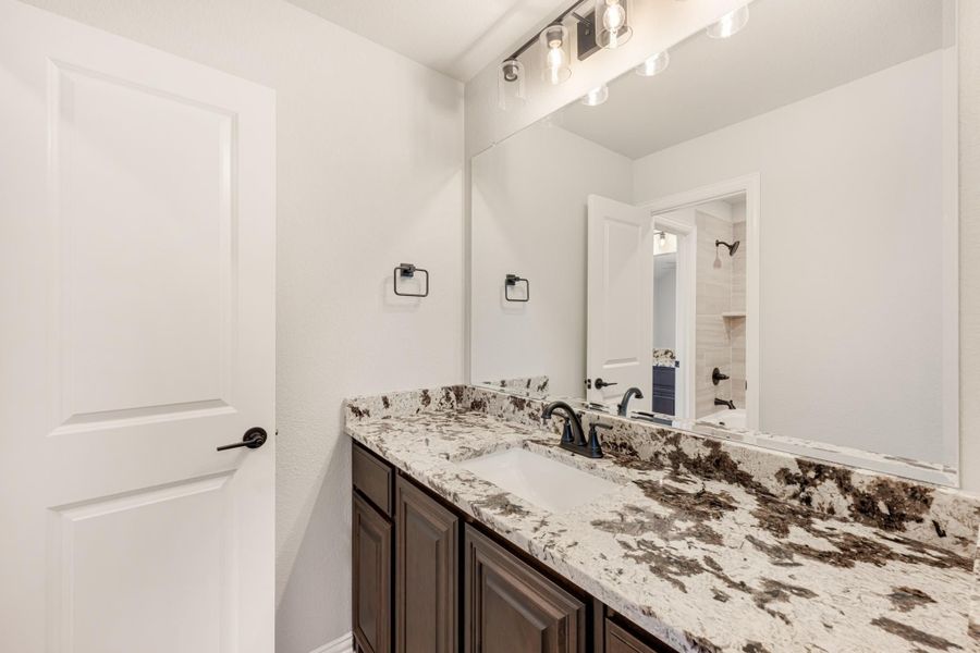 Bathroom vanity with granite countertop, dark wood cabinets, single sink, and large mirror with overhead lighting. Bathroom vanity with granite countertop, dark wood cabinets, single sink, and large mirror with overhead lighting.