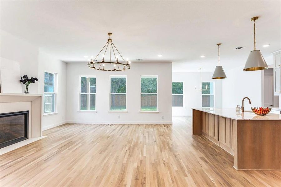 Kitchen with a chandelier, healthy amount of natural light, light wood-style floors, a glass covered fireplace, and recessed lighting