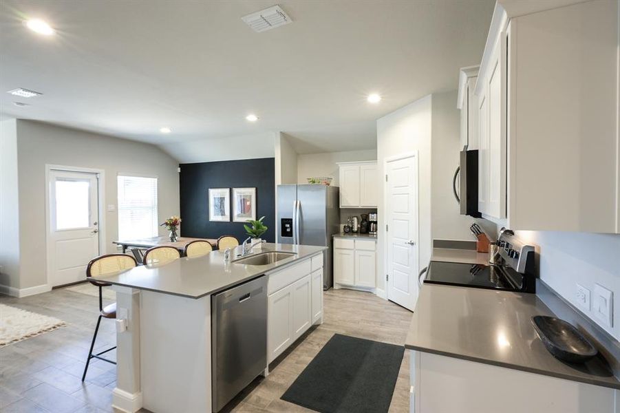 Kitchen with a center island with sink, a breakfast bar area, stainless steel appliances, visible vents, and white cabinets