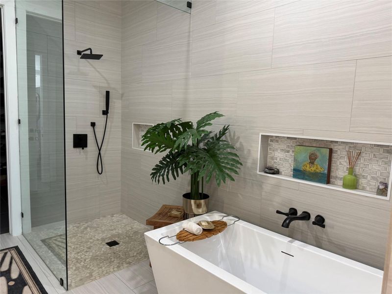 Spacious bathroom featuring a freestanding soaking tub with wall-mounted matte black faucet, a walk-in shower with glass enclosure and pebble floor, and large format wall tiling