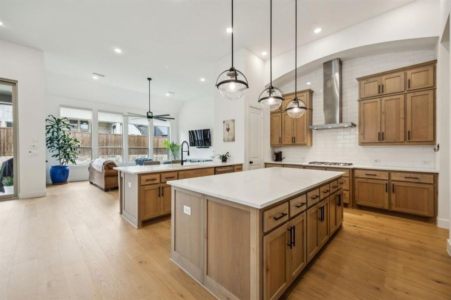 Kitchen with a kitchen island, wall chimney range hood, stainless steel gas stovetop, light wood finished floors, and light countertops