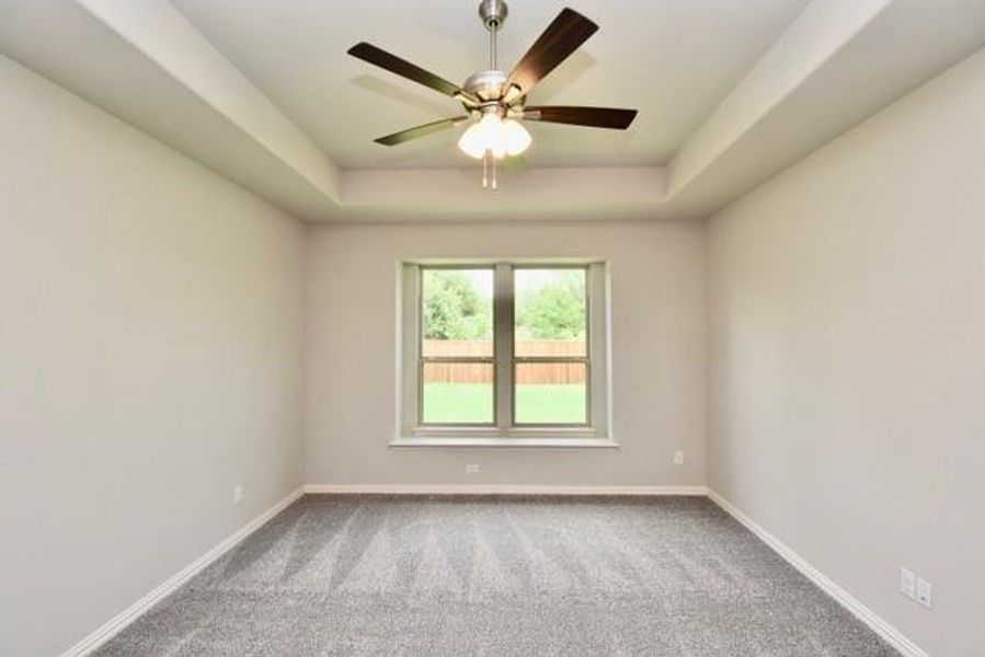 Carpeted bedroom with a raised ceiling, ceiling fan, and boxed window seat