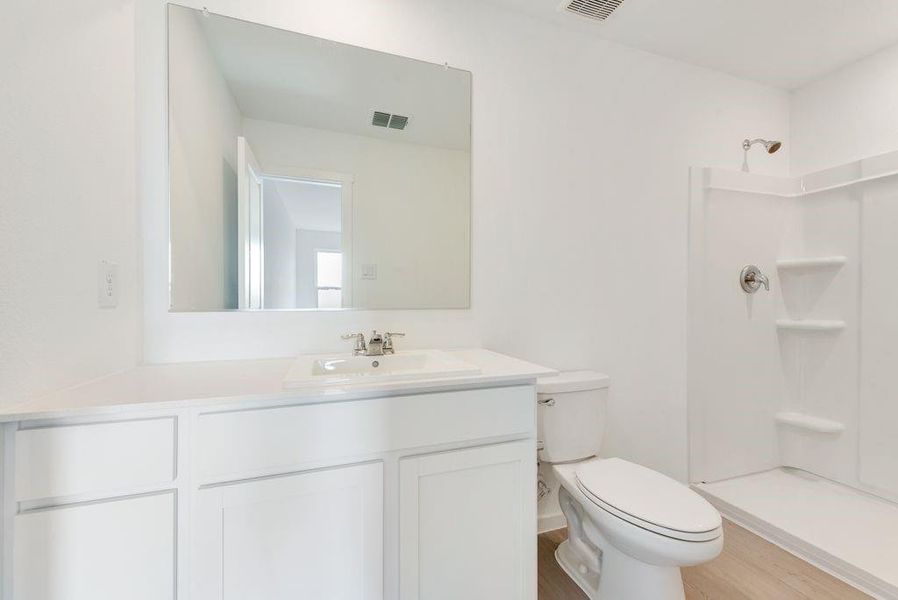 Bathroom with toilet, wood finished floors, vanity, visible vents, and a shower