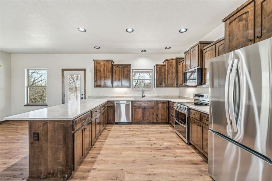 Kitchen featuring light wood-style flooring, a peninsula, stainless steel appliances, recessed lighting, and a sink
