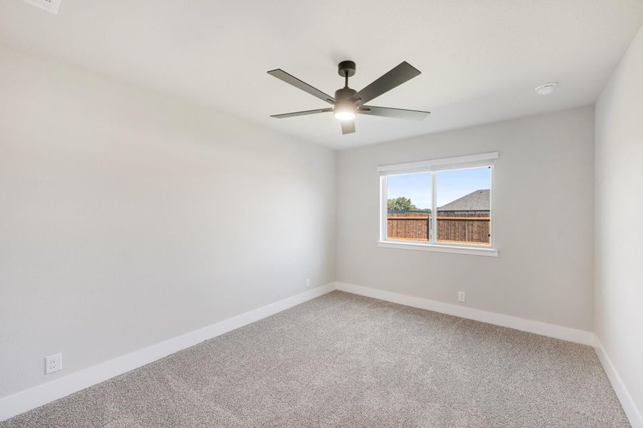 Empty bedroom with gray carpet, ceiling fan, and single window with backyard view