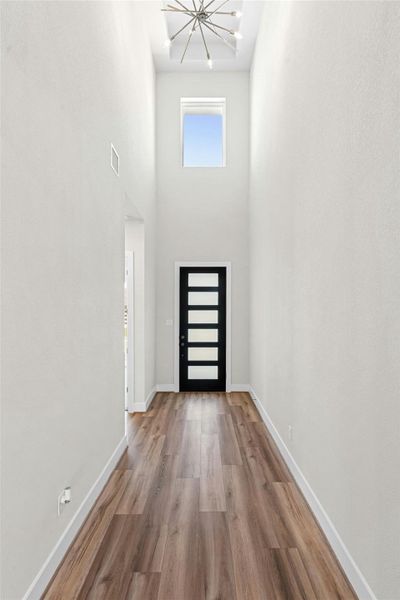 Foyer entrance with wood finished floors, a chandelier, and a towering ceiling
